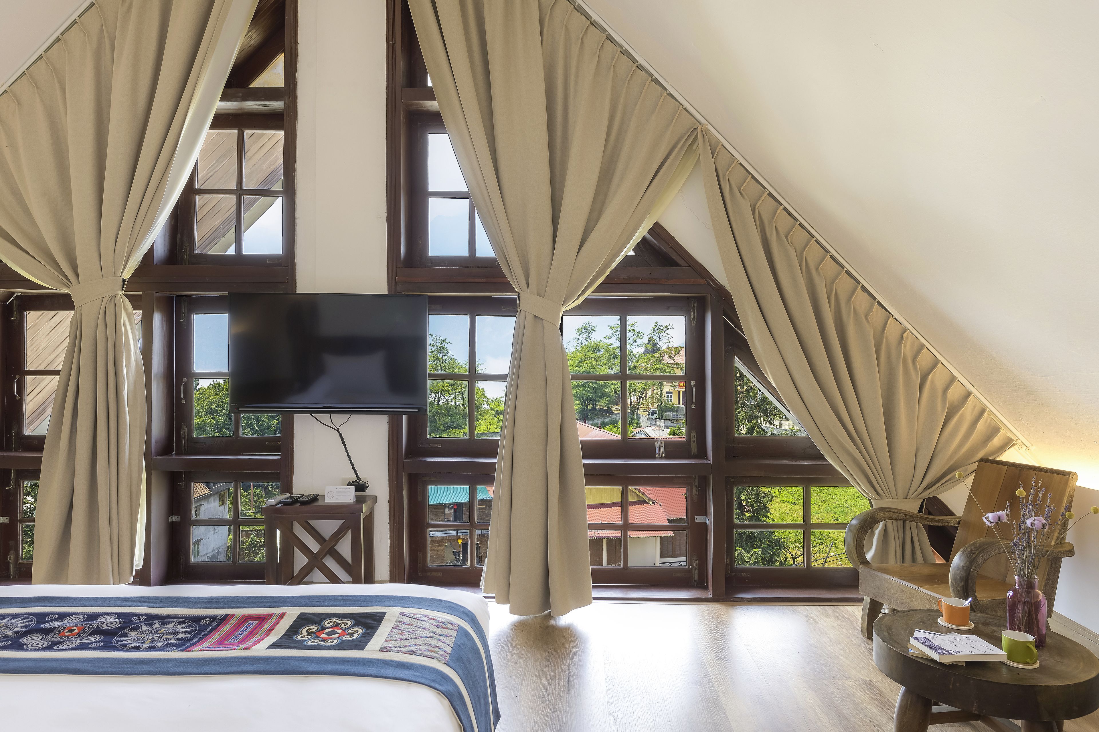 Un dormitorio con una cama grande, televisión, una mesita con un florero y vistas a zonas verdes.