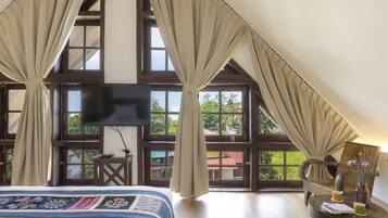Un dormitorio con una cama grande, televisión, una mesita con un florero y vistas a zonas verdes.