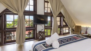Habitación de hotel con una cama grande, un televisor de pantalla plana y vistas a un paisaje verde a través de amplias ventanas.