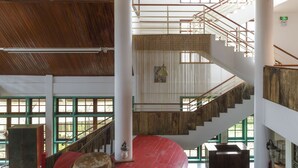 Un interior de varios niveles con vigas de madera, una plataforma circular roja y una escalera con barandillas de metal.