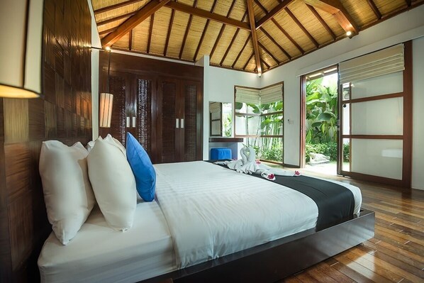 A spacious bedroom with a large bed, wooden ceiling, and a view of lush greenery outside.