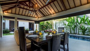 An outdoor dining area with a table set for four, surrounded by chairs, under a wooden ceiling with a fan.