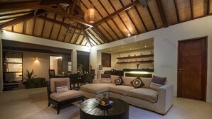A spacious living area with a high ceiling, a round coffee table, a beige sofa, and a dining area in the background.
