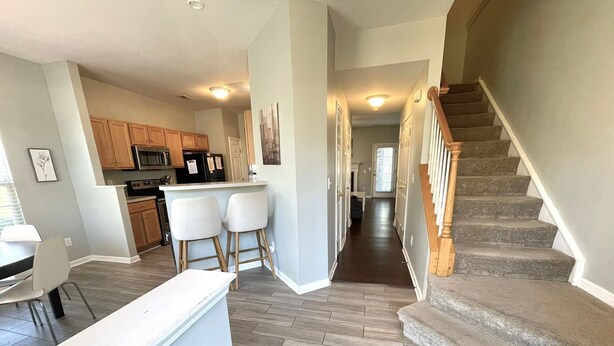 A modern kitchen with wooden cabinets, a central island with bar stools, and a staircase leading to another level. - University townhome,  available for long-term. (Charlotte)