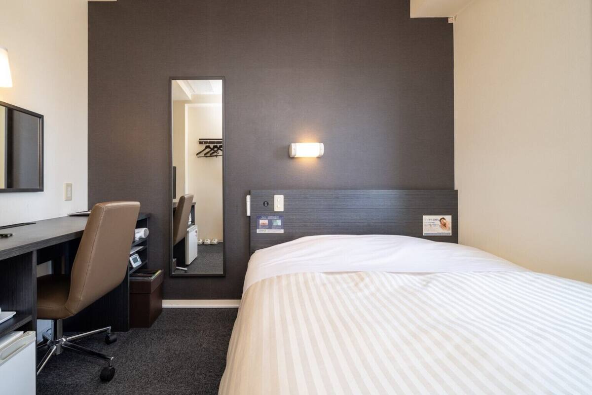 Een hotelkamer met een bed, een bureau, een stoel, een spiegel en een wandlamp.