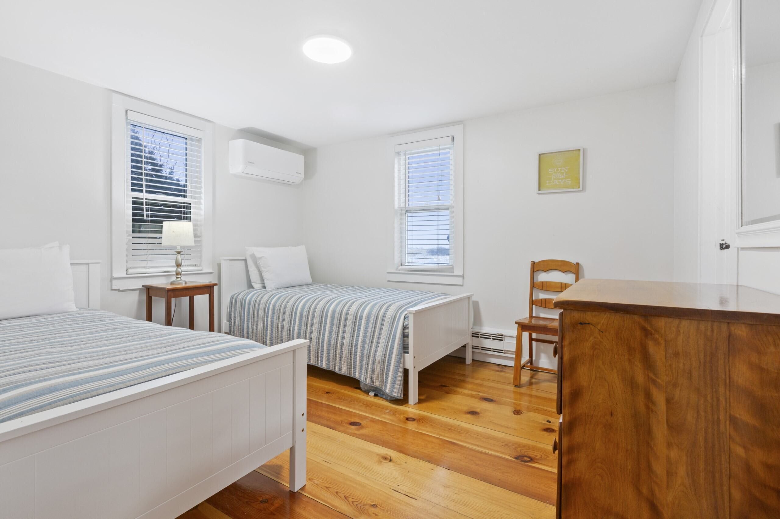 A bedroom with two beds, a wooden dresser, a chair, and a small table.