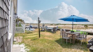 Eine Terrasse im Freien mit Tisch und Stühlen, einem blauen Sonnenschirm und Blick auf den Strand.
