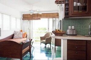 Cozy retreat with a bed, chair, and kitchenette, featuring a window with blinds and a ceiling fan.