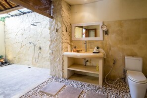 A bathroom with a stone wall, a sink with a mirror, a toilet, and a shower area. - Best Location! 3BD Villa, Central Seminyak! - 3Min Walk To Eat Street! W/Pool! (seminyak)