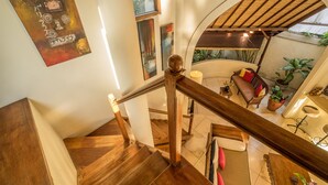 Un escalier en bois mène à un espace de vie comprenant un canapé, des plantes et une lampe.