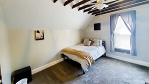 A bedroom with a sloped ceiling, a bed with striped bedding, a ceiling fan, a window with curtains, and a small picture on the wall. - Experience Indianapolis living close to Lucas Oil Stadium (Indianapolis)