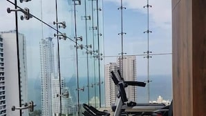 A gym with exercise equipment and a city view through large glass windows. - Riviera Pattaya Beach (Pattaya)