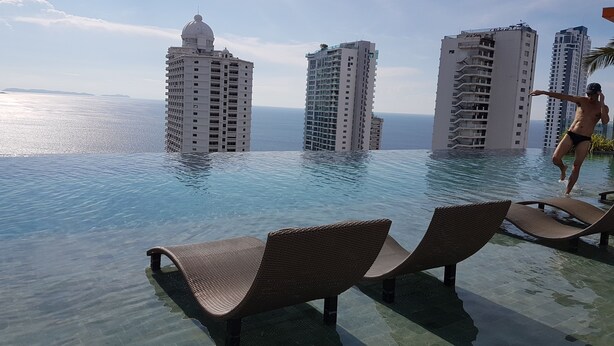 An infinity pool with lounge chairs, overlooking tall buildings and the ocean. - Riviera Pattaya Beach (Pattaya)