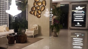 A modern lobby with a chandelier, a seating area with a sofa and armchairs, a decorative wall, and a digital display. - Riviera Pattaya Beach (Pattaya)