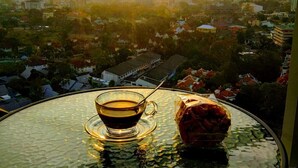 A table with a glass of coffee and a pastry, overlooking a cityscape during sunset. - Riviera Pattaya Beach (Pattaya)