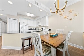 A modern kitchen with white cabinetry, a central island, and a dining area with a wooden table and white chairs.