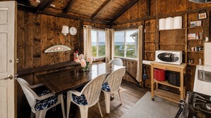 Interior rústico de madera con una mesa de comedor, sillas, una zona de cocina con microondas y vistas al exterior.