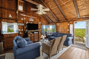 A wooden cabin interior with a TV, two sofas, a coffee table, and a ceiling fan.