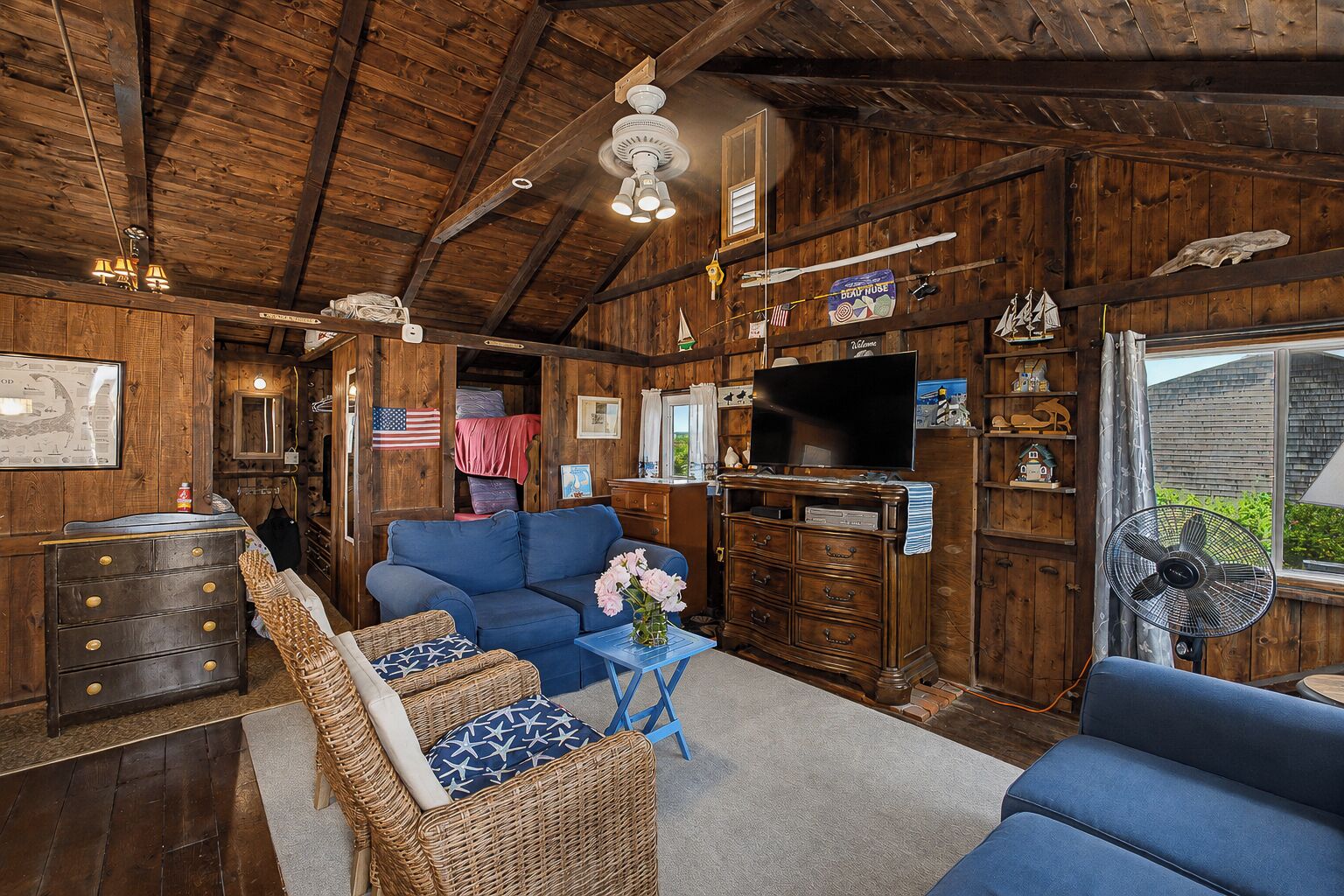 Un interno rustico con soffitto in legno, una televisione, mobili in vimini e un tavolino con fiori.