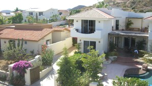 A residential area with a house featuring a balcony, a swimming pool, and a hilly landscape in the background.