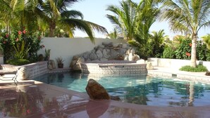 A pool with a stone wall and palm trees.