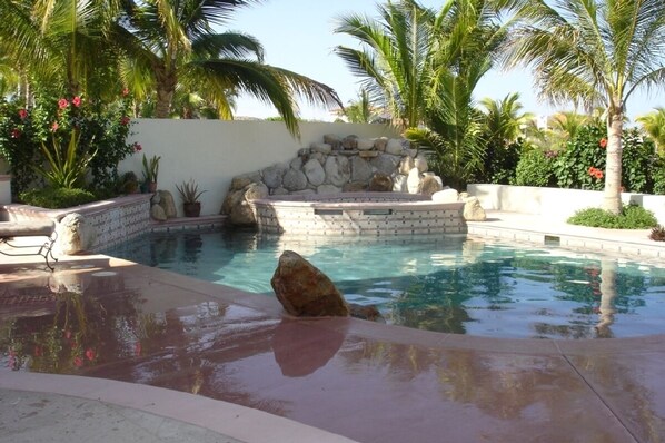 Relax by the serene pool surrounded by lush greenery and a soothing waterfall.