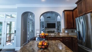 A kitchen with a granite countertop, wooden cabinets, a stainless steel refrigerator, and a fruit bowl. - Luxury Secluded Family Retreat (Apex)
