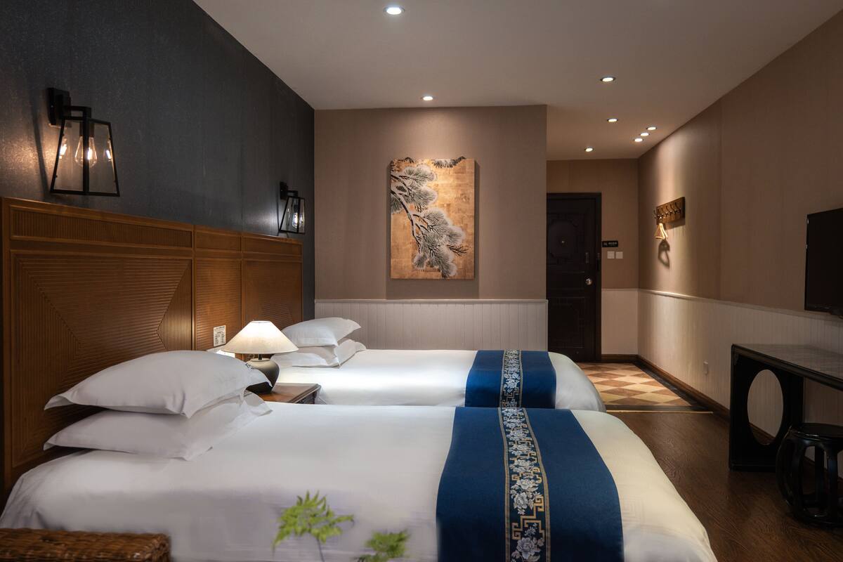 A hotel room with two beds, a wooden headboard, a wall-mounted artwork, a desk, and a television.
