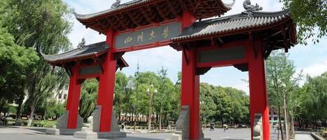 A traditional red gate with Chinese characters, set in a park with trees and a clear sky.