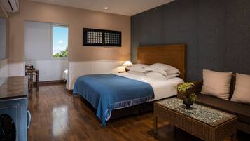 Habitación de hotel con cama, sofá, una mesita con planta, ventana y aire acondicionado instalado en la pared.