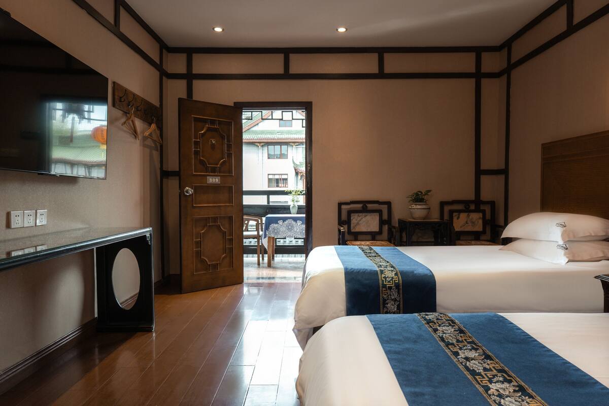 A hotel room with two beds, a television, a wooden door, and a view of the outside.
