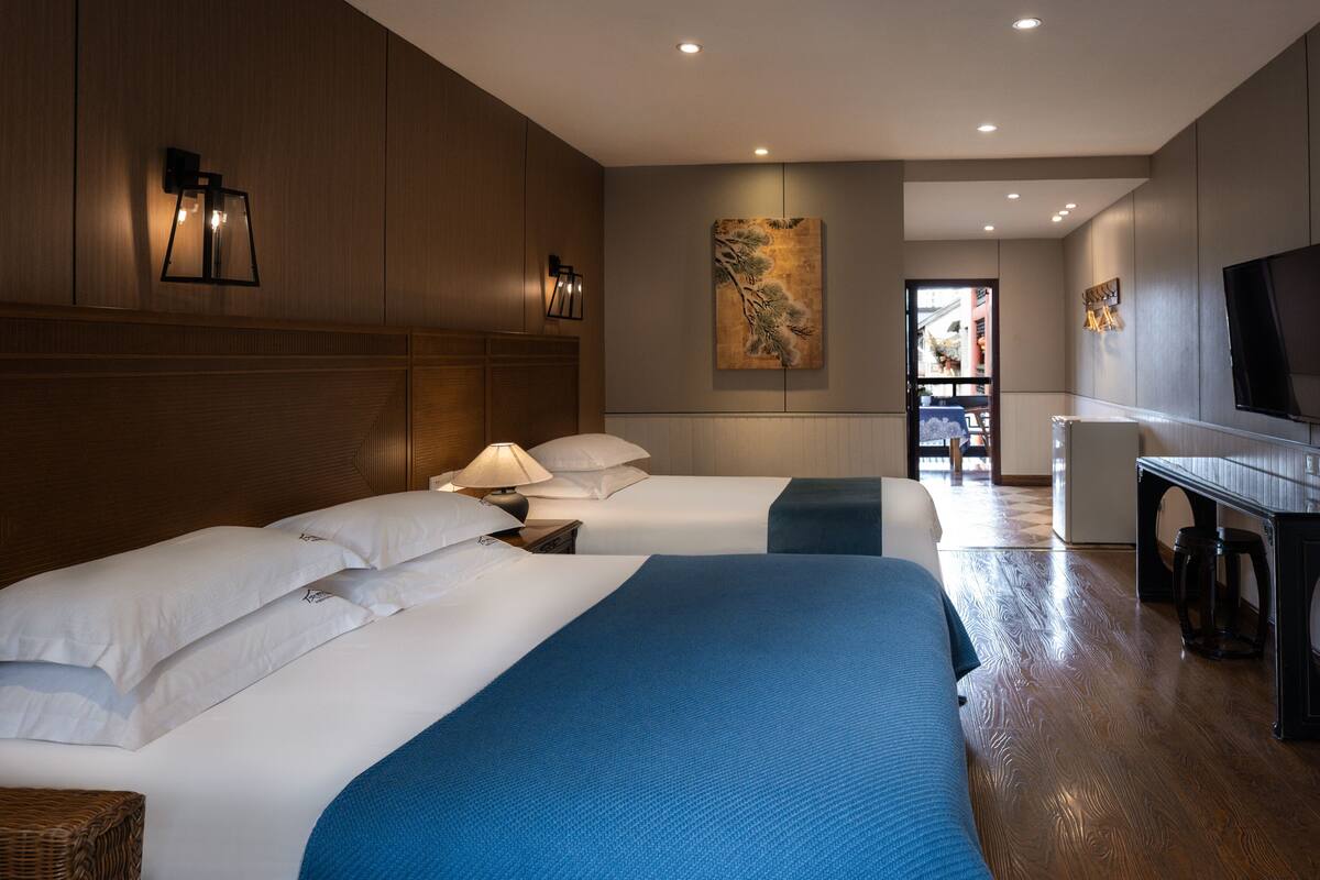 A hotel room with two beds, a desk, a television, and a painting on the wall.
