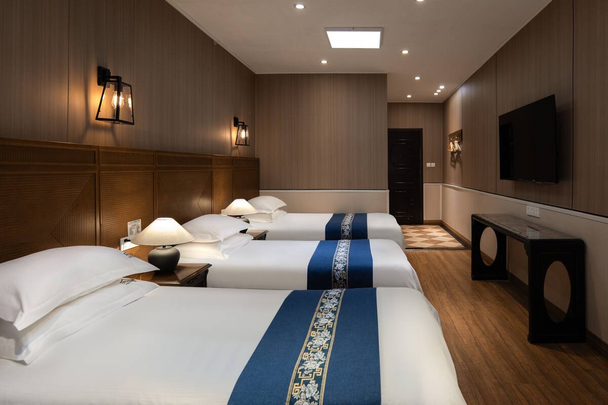 A hotel room with four beds, a TV, a desk, and a lamp.