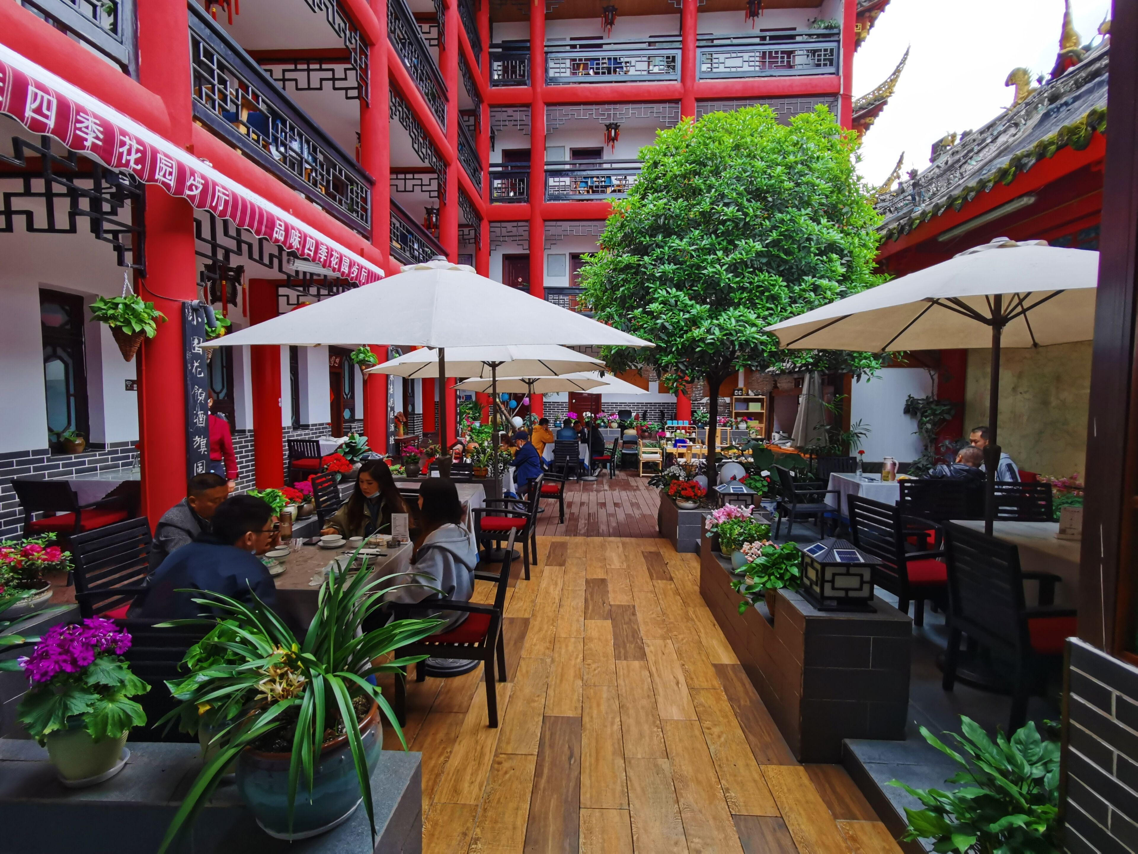 An indoor courtyard with wooden flooring, red pillars, and multiple tables and chairs.