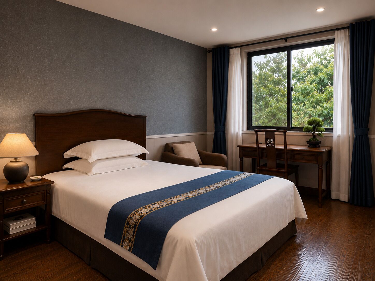 A hotel room with a bed, bedside table, lamp, chair, desk, and window with curtains.