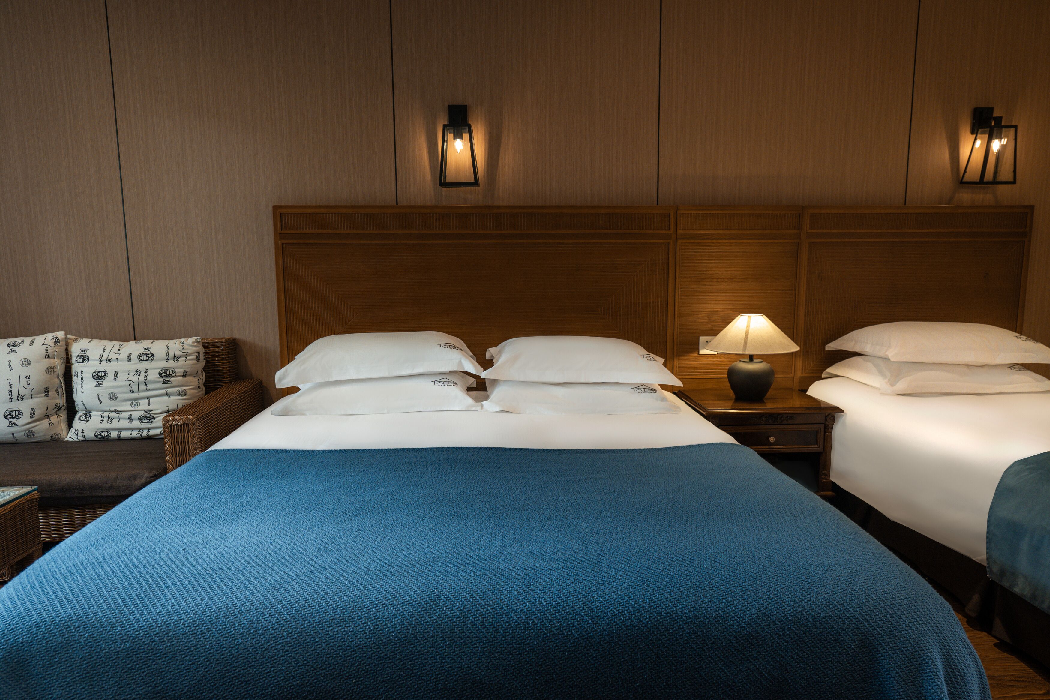 Une chambre d’hôtel avec un grand lit, deux tables de chevet, une lampe et un luminaire fixé au mur.