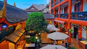 Un edificio tradicional con patio central, que cuenta con un comedor con mesas y sombrillas, rodeado de abundante vegetación.