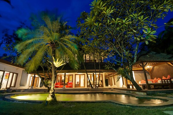 A well-lit resort with a swimming pool, outdoor seating, and lush greenery.