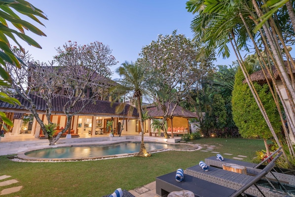 Zona junto a la piscina con sillones de descanso, una piscina y una casa con tejado de tejas.