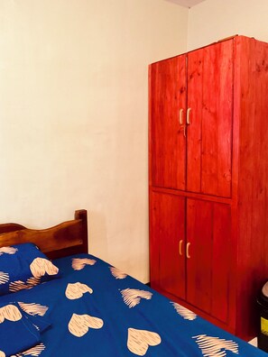 Ein Zimmer mit einem Bett, einem Holz-Kopfteil, einer blauen Tagesdecke mit Herzmuster und einem roten Kleiderschrank.