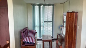 Un coin repas avec une table en bois, des chaises, un banc doté d’un coussin à rayures et une vue sur l’extérieur par une fenêtre ornée de rideaux.