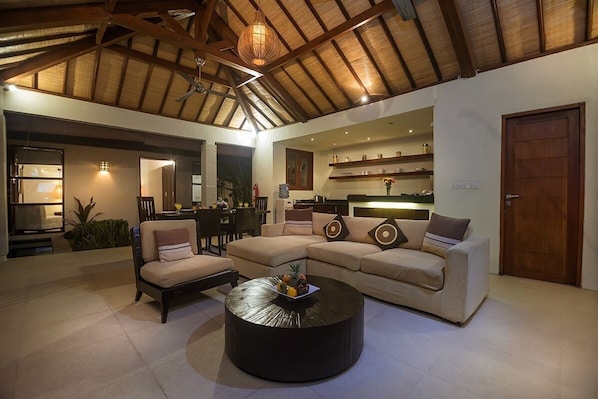 A spacious living area with a high ceiling, a round coffee table, a beige sofa, and a dining area in the background. - 5 Bdr -Last Minute Deal 50%+ OFF!!! (Legian)