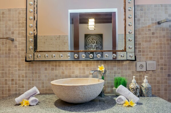 A bathroom with a large mirror, a stone sink, towels, and toiletries.