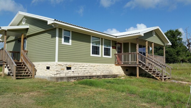 A two-story house with a stone foundation, green siding, and a covered porch with wooden stairs.