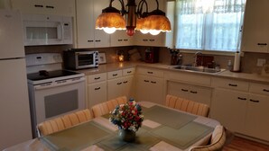 A kitchen with white cabinets, a microwave, a toaster, a stove, and a sink. There is a table with a vase of flowers and a chair.