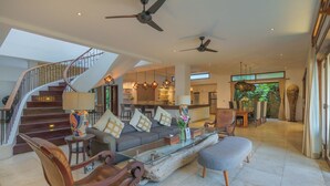 A spacious living area with a staircase, modern furniture, and a large window offering a view of the outdoors. - Beach Club House, 7 Bdrm, Close To Beach, Sunsets (Canggu)