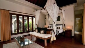 A luxurious bedroom with a canopy bed, a glass coffee table, and a view of a garden through large windows. - Beach Club House, 7 Bdrm, Close To Beach, Sunsets (Canggu)