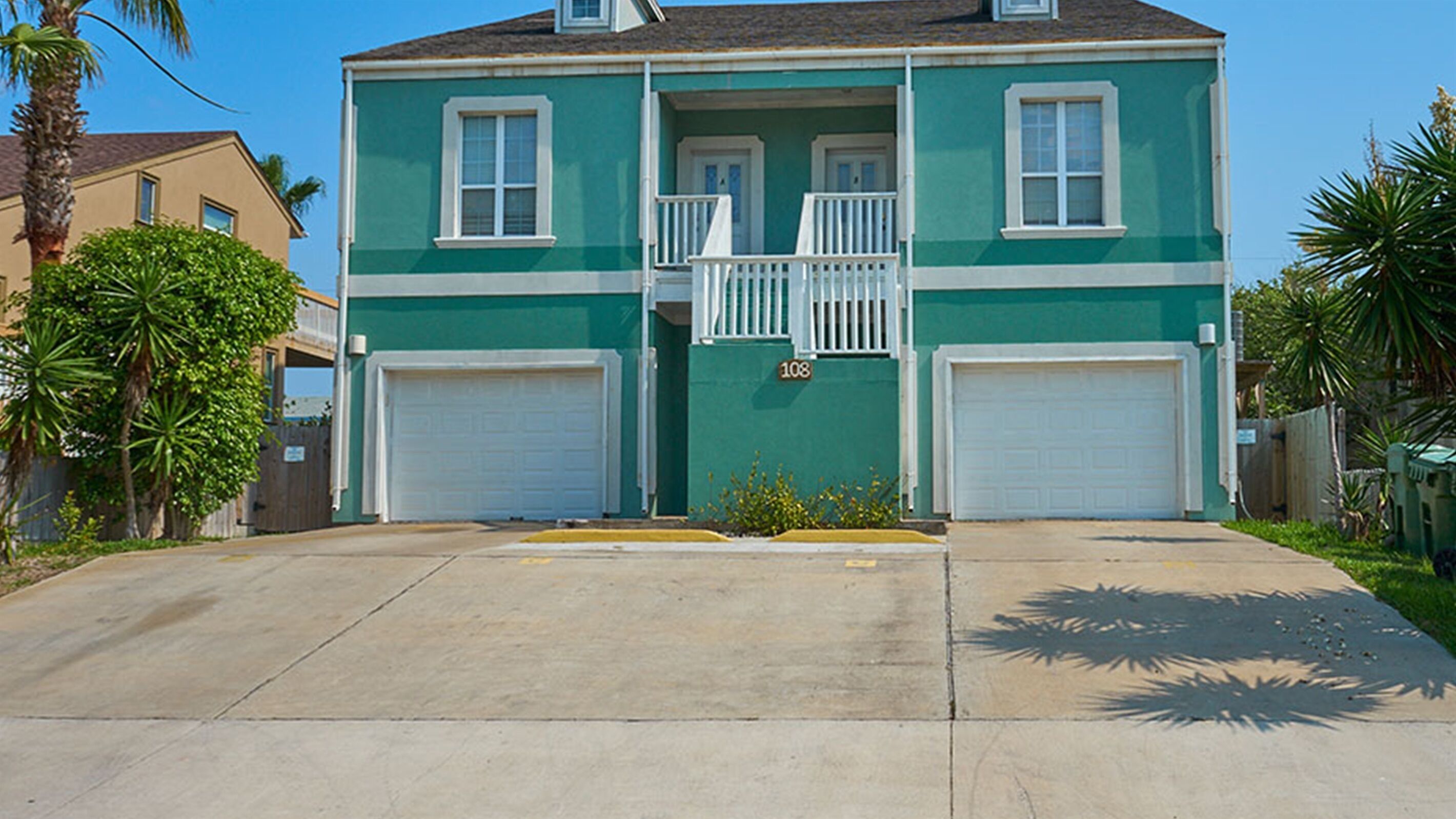 A two-story residential building with a green facade, two garage doors, and a small balcony.