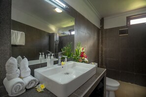 A modern bathroom with a large sink, a mirror, and a toilet. There are towels and toiletries on the counter.