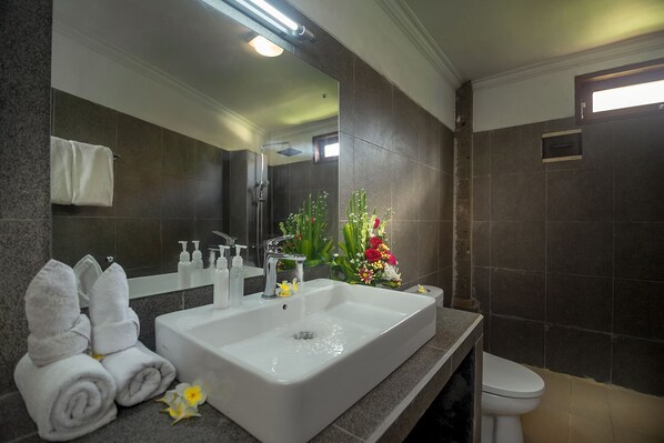 Un baño moderno con un lavamanos grande, un espejo y un inodoro. Hay toallas y artículos de aseo en la encimera.